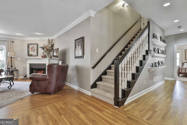 staircase featuring a healthy amount of sunlight, baseboards, a lit fireplace, and wood finished floors