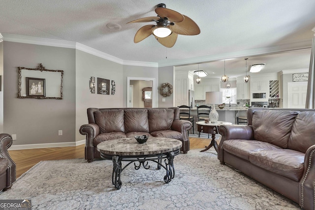 living room featuring light wood-type flooring, ornamental molding, a ceiling fan, a textured ceiling, and baseboards