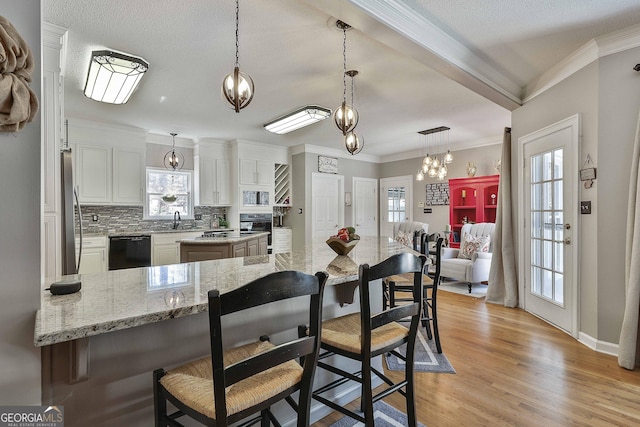 kitchen with a sink, black appliances, white cabinets, a kitchen bar, and backsplash