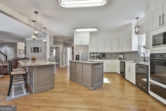 kitchen with a sink, decorative backsplash, black appliances, white cabinets, and a center island