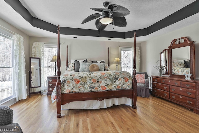 bedroom with a textured ceiling, a raised ceiling, a ceiling fan, and wood finished floors