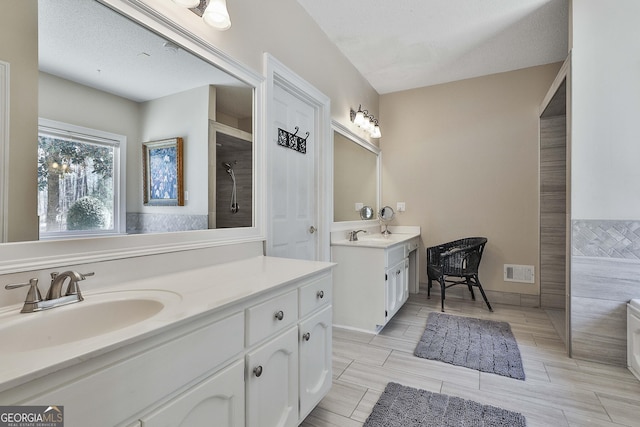 bathroom featuring a sink, visible vents, two vanities, and a tile shower