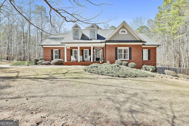 view of front of home featuring brick siding, covered porch, and fence