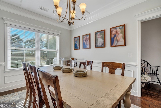 dining space featuring visible vents, a decorative wall, ornamental molding, wood finished floors, and a notable chandelier