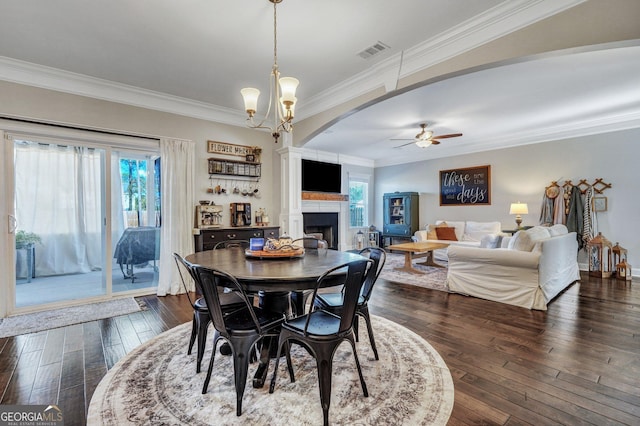 dining area featuring visible vents, ornamental molding, ceiling fan with notable chandelier, a fireplace, and dark wood-style flooring