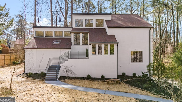 mid-century modern home with fence, roof with shingles, and stucco siding