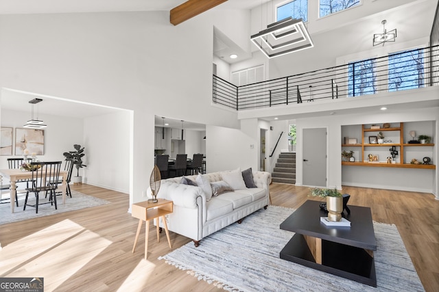 living area featuring beam ceiling, plenty of natural light, stairs, and wood finished floors