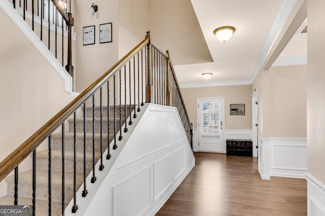 staircase with crown molding, a decorative wall, wood finished floors, and a wainscoted wall