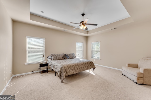 carpeted bedroom featuring baseboards, ceiling fan, a tray ceiling, and visible vents