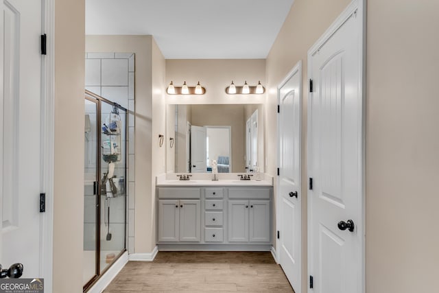 bathroom featuring double vanity, a shower stall, a sink, and wood finished floors
