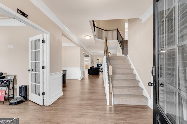 foyer entrance with french doors, crown molding, a wainscoted wall, light wood finished floors, and stairs