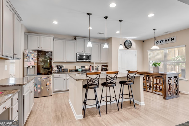 kitchen with a kitchen breakfast bar, a center island, stainless steel appliances, light wood-type flooring, and visible vents