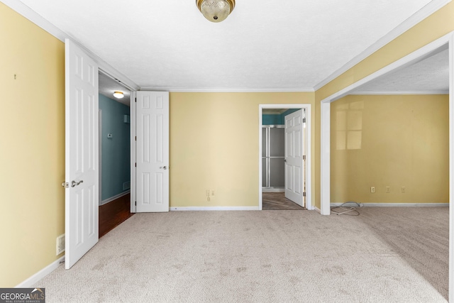 unfurnished bedroom featuring a closet, carpet, crown molding, baseboards, and a spacious closet