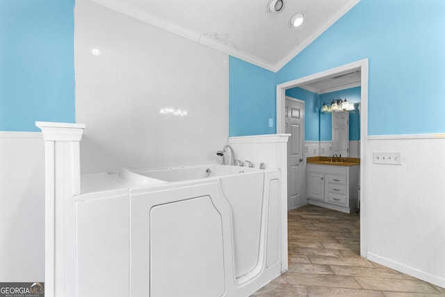 laundry room with wood finish floors, a wainscoted wall, ornamental molding, a textured ceiling, and a sink