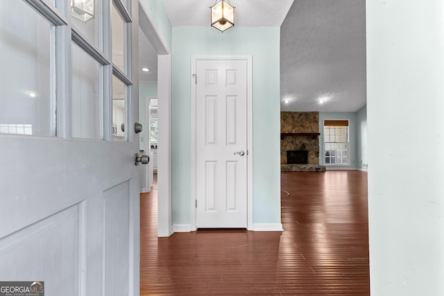 foyer entrance with a fireplace, wood finished floors, baseboards, and a textured ceiling