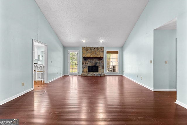 unfurnished living room featuring hardwood / wood-style floors, lofted ceiling, a stone fireplace, and a textured ceiling