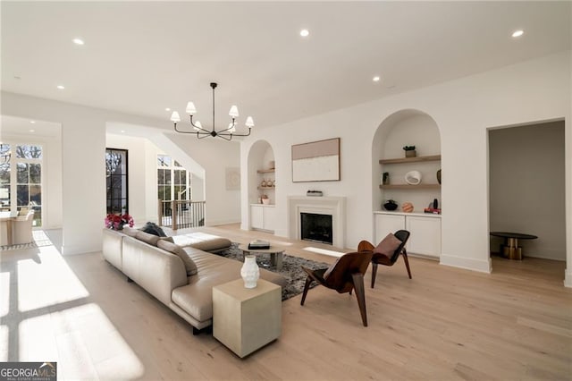 living room featuring built in features, an inviting chandelier, recessed lighting, a fireplace, and light wood-style floors