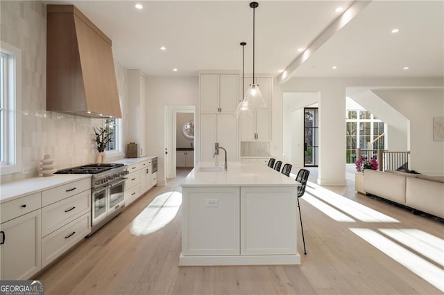 kitchen featuring custom range hood, a sink, double oven range, open floor plan, and light wood-style floors