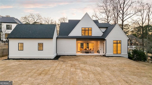 back of house at dusk with a patio and a shingled roof