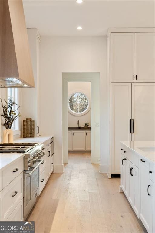 kitchen with wall chimney range hood, recessed lighting, double oven range, and white cabinets