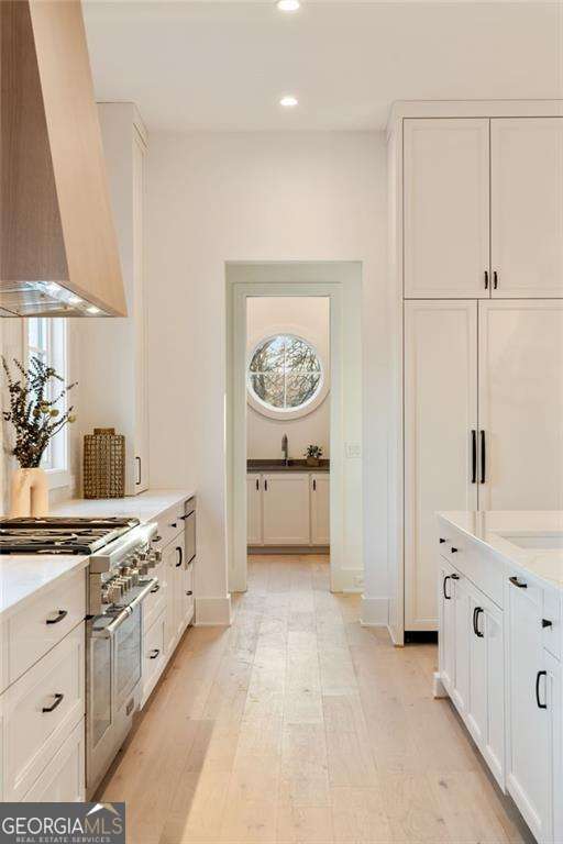 kitchen featuring range with two ovens, wall chimney exhaust hood, white cabinets, and light countertops