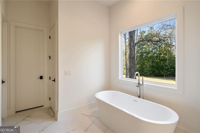 bathroom featuring marble finish floor, baseboards, and a freestanding tub