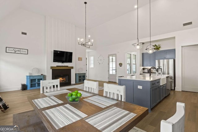 dining area with wood finished floors, baseboards, visible vents, high vaulted ceiling, and a large fireplace