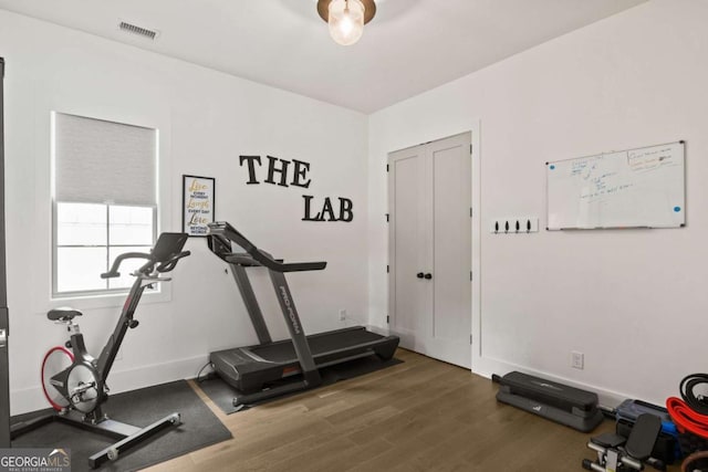 exercise room with wood finished floors, visible vents, and baseboards