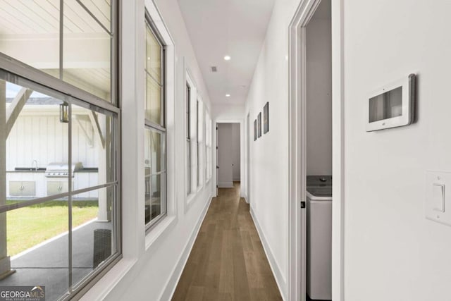 corridor featuring a sink, wood finished floors, recessed lighting, baseboards, and washer / dryer