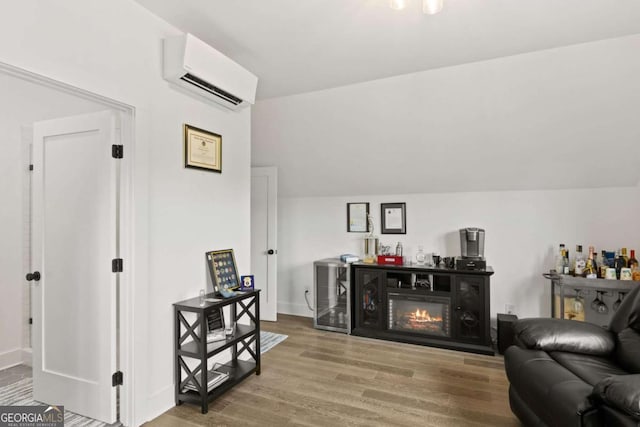 living room featuring wood finished floors, baseboards, vaulted ceiling, a wall mounted air conditioner, and a glass covered fireplace