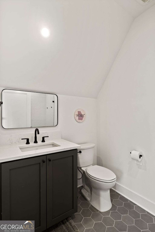 bathroom with baseboards, toilet, vaulted ceiling, tile patterned floors, and vanity