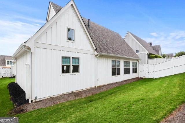rear view of house featuring a lawn, board and batten siding, a shingled roof, and fence