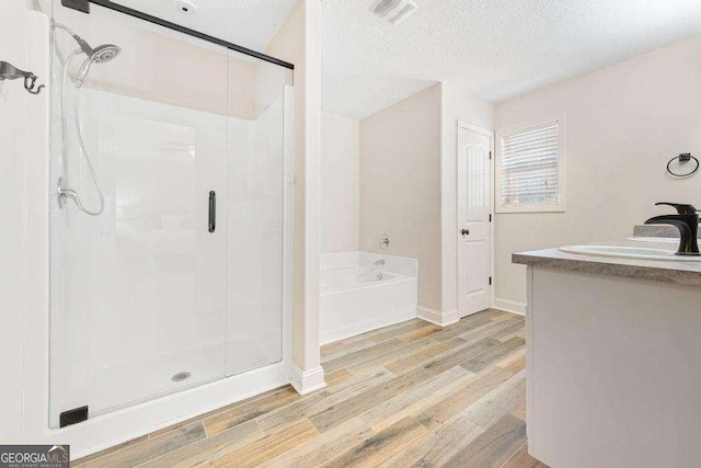 bathroom with a shower stall, a bath, wood finished floors, and visible vents