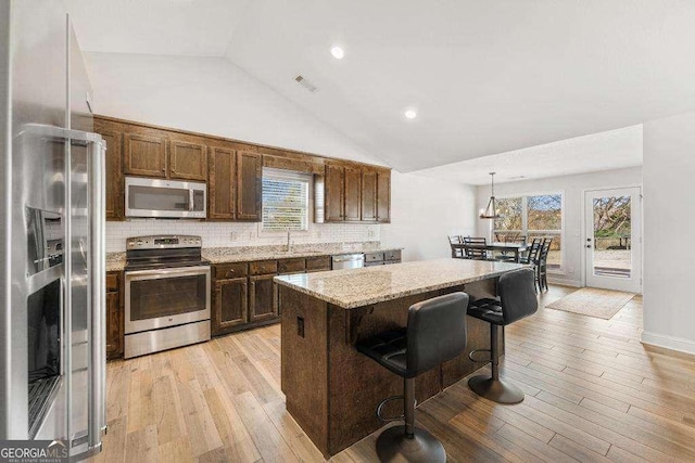 kitchen with light wood-type flooring, a kitchen island, appliances with stainless steel finishes, decorative backsplash, and light stone countertops