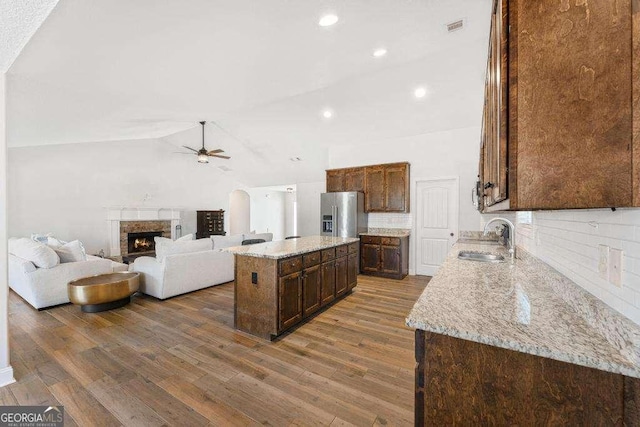 kitchen featuring ceiling fan, a warm lit fireplace, dark wood-style floors, stainless steel fridge, and a sink