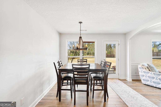 dining area with a textured ceiling, wood finished floors, arched walkways, and a chandelier