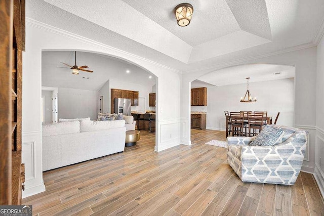 living area with light wood-style flooring, arched walkways, a textured ceiling, a decorative wall, and ceiling fan with notable chandelier