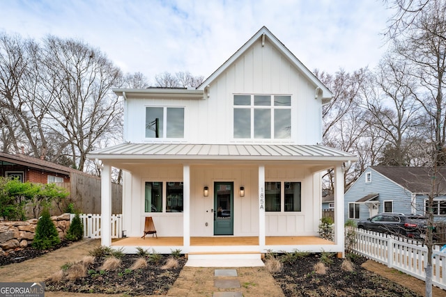 modern farmhouse with fence, covered porch, board and batten siding, and a standing seam roof