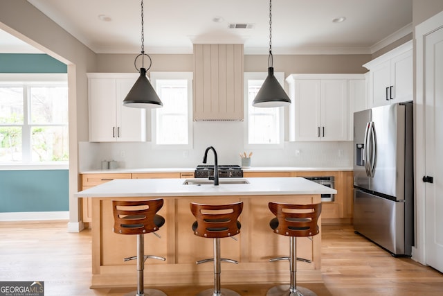 kitchen featuring visible vents, an island with sink, light countertops, ornamental molding, and stainless steel fridge