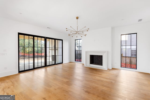 unfurnished living room with a notable chandelier, light wood finished floors, and visible vents