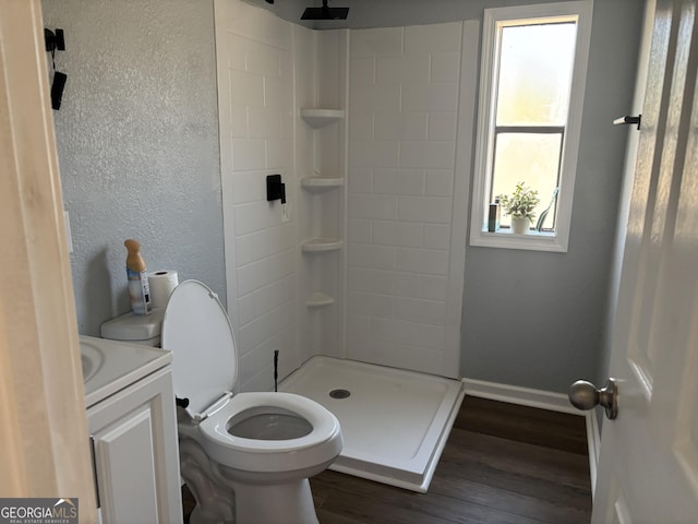 full bathroom with vanity, wood finished floors, a shower stall, toilet, and a textured wall