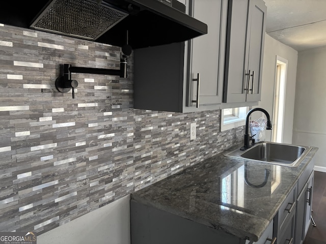 kitchen with backsplash, gray cabinetry, ventilation hood, dark stone countertops, and a sink