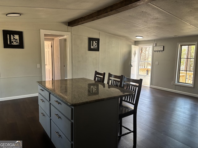 kitchen featuring a kitchen island, vaulted ceiling with beams, dark wood finished floors, dark stone counters, and a breakfast bar