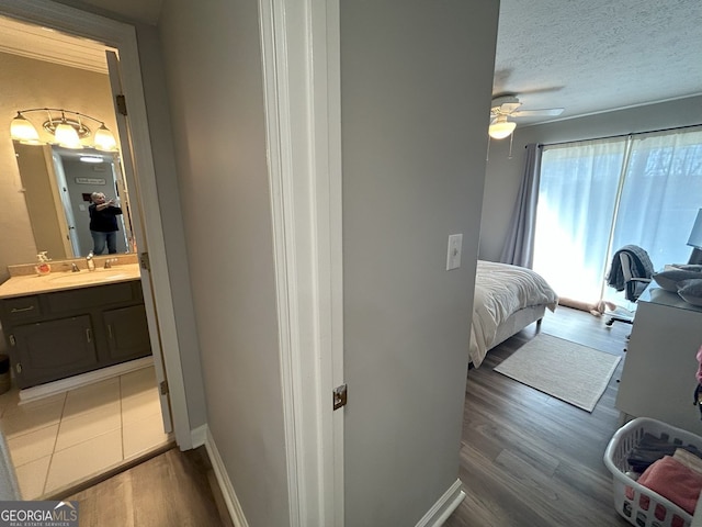 bedroom featuring baseboards, wood finished floors, a textured ceiling, a ceiling fan, and a sink