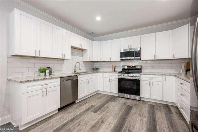 kitchen with a sink, stainless steel appliances, wood finished floors, and white cabinets