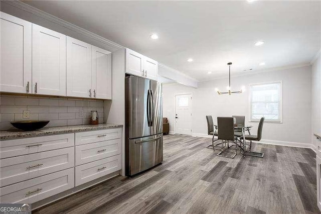 kitchen featuring dark wood-type flooring, light stone counters, white cabinetry, freestanding refrigerator, and decorative backsplash