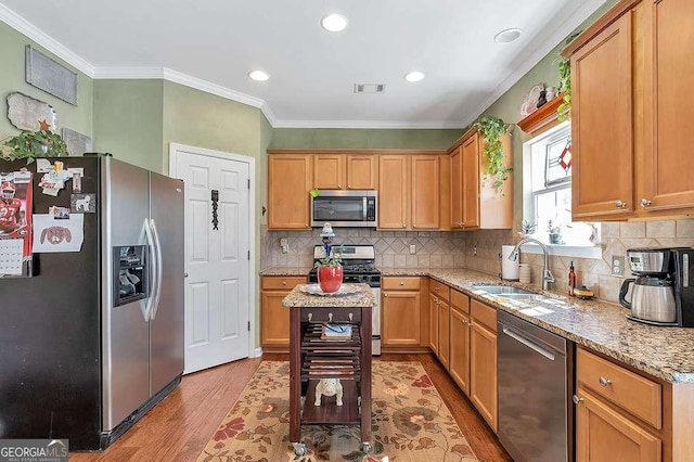 kitchen with stainless steel appliances, a sink, visible vents, wood finished floors, and ornamental molding