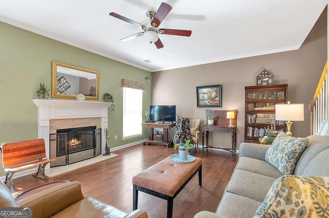 living room featuring wood finished floors, crown molding, baseboards, a fireplace, and ceiling fan