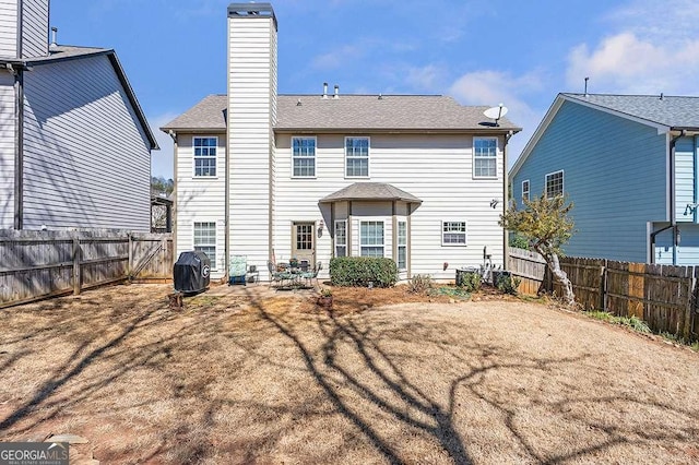 rear view of property featuring a fenced backyard, a chimney, and a shingled roof