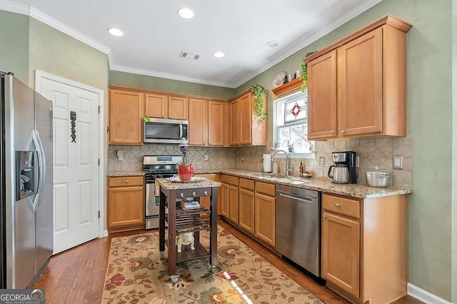 kitchen with stainless steel appliances, a sink, visible vents, wood finished floors, and crown molding